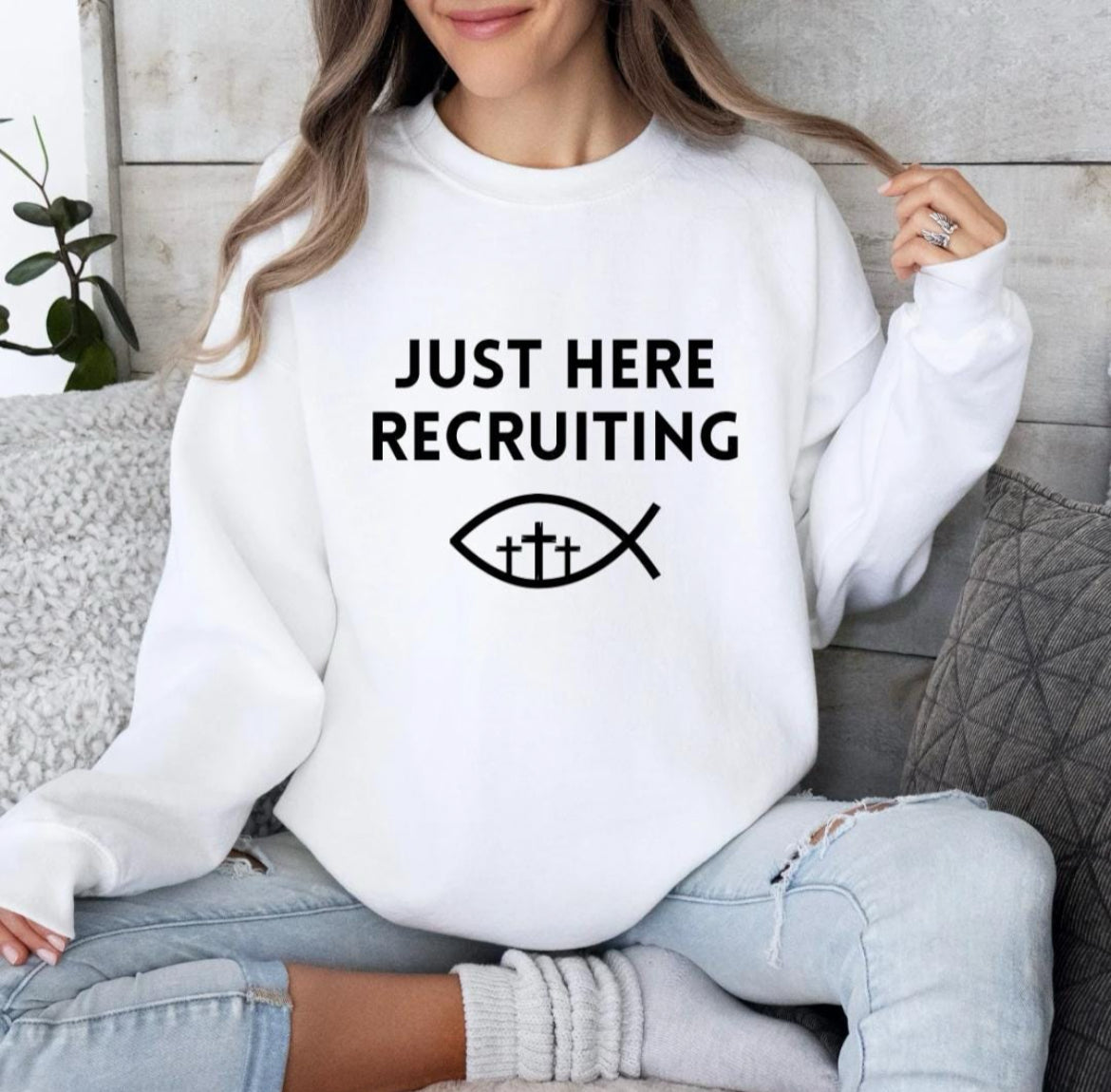 White crewneck sweatshirt that say, "Just here recruiting" with the ichthus fish symbol with three crosses inside the fish.