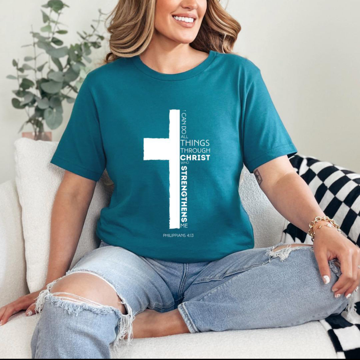 Deep teal crewneck t-shirt with a cross where half of the cross is the Bible verse Philippians 4:13. It says, “I can do all things through Christ who strengthens me.”