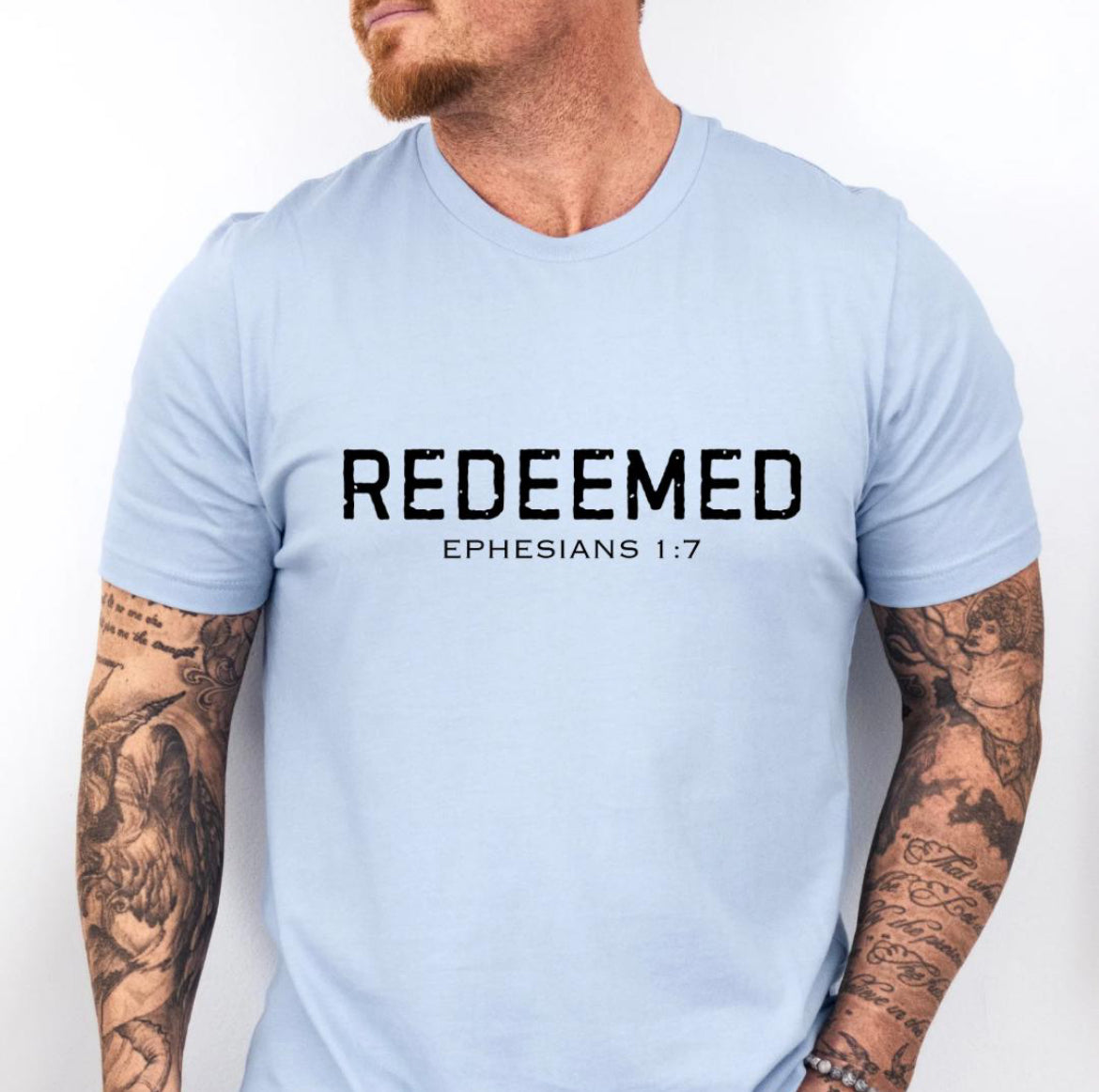 Baby blue Crewneck t-shirt that says, “redeemed” in large distressed letters. Underneath in smaller letters it says, “Ephesians 1 7.”