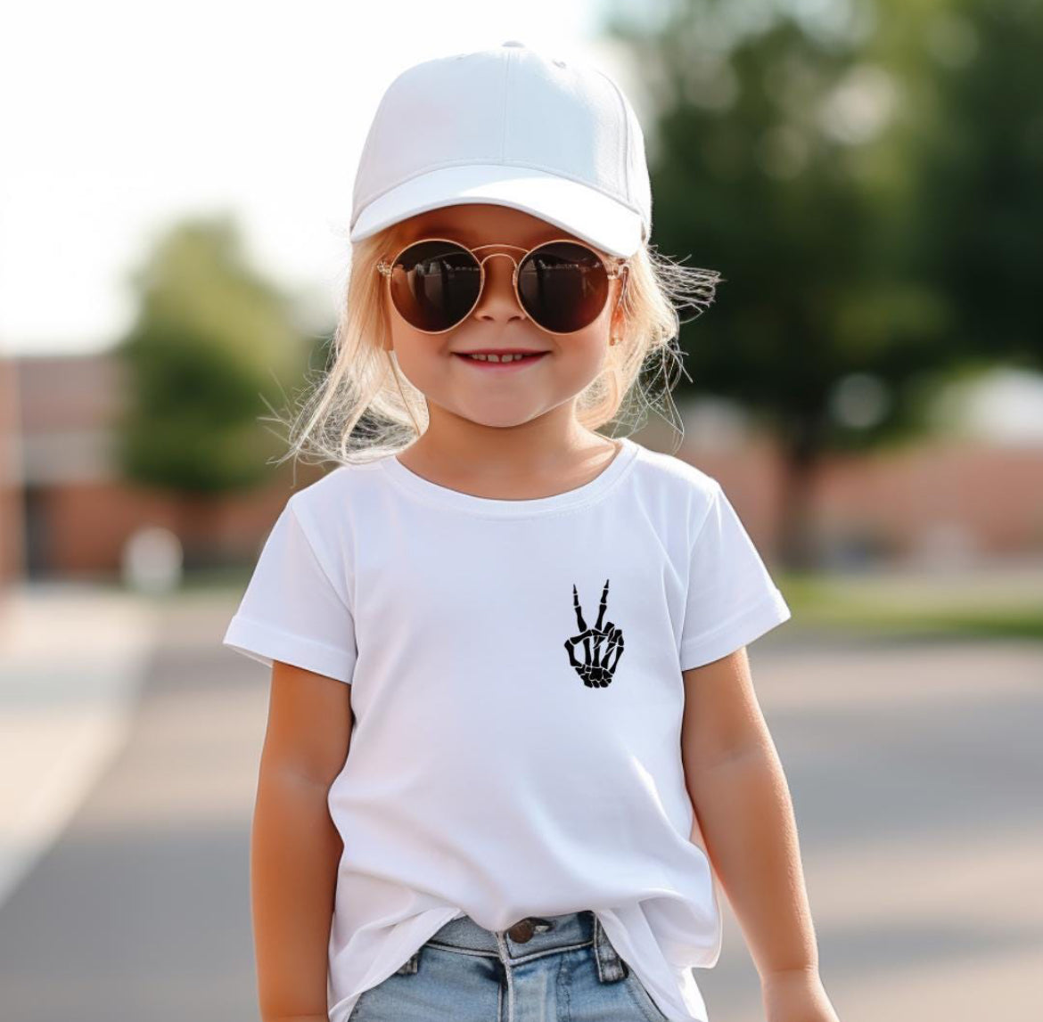 White Crewneck t-shirt that has a peace sign hand symbol made of bones in the upper left hand corner. On the back it says, “God is within her she will not fail.” Underneath in smaller letters it says, “Psalm 46 5.”