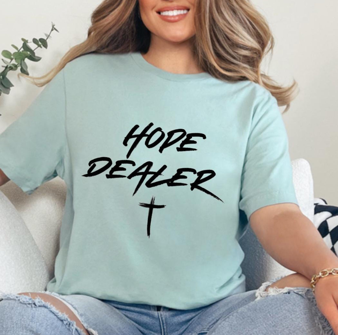 Dusty green crewneck t-shirt that says, “Hope dealer” in an urban graffiti style writing with a cross. 