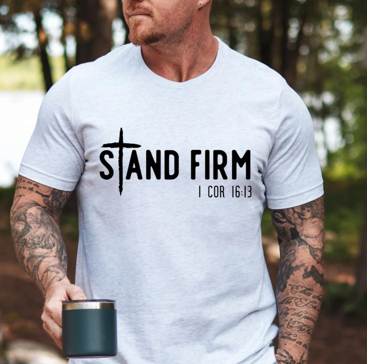 Ash white Crewneck t-shirt that says, “Stand Firm” in large letters. The “t” in stand is a cross. Underneath in smaller letters it says, “1 Corinthians 16:13”.