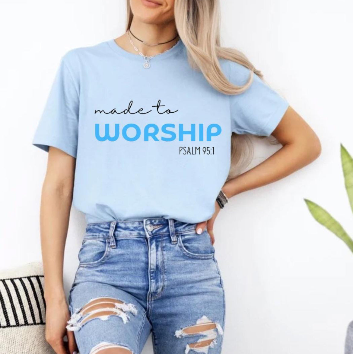 Baby blue crewneck t-shirt that says, “made to worship” where the word “worship” is bold and blue. Underneath in smaller letters it says, “psalm 95 1.”