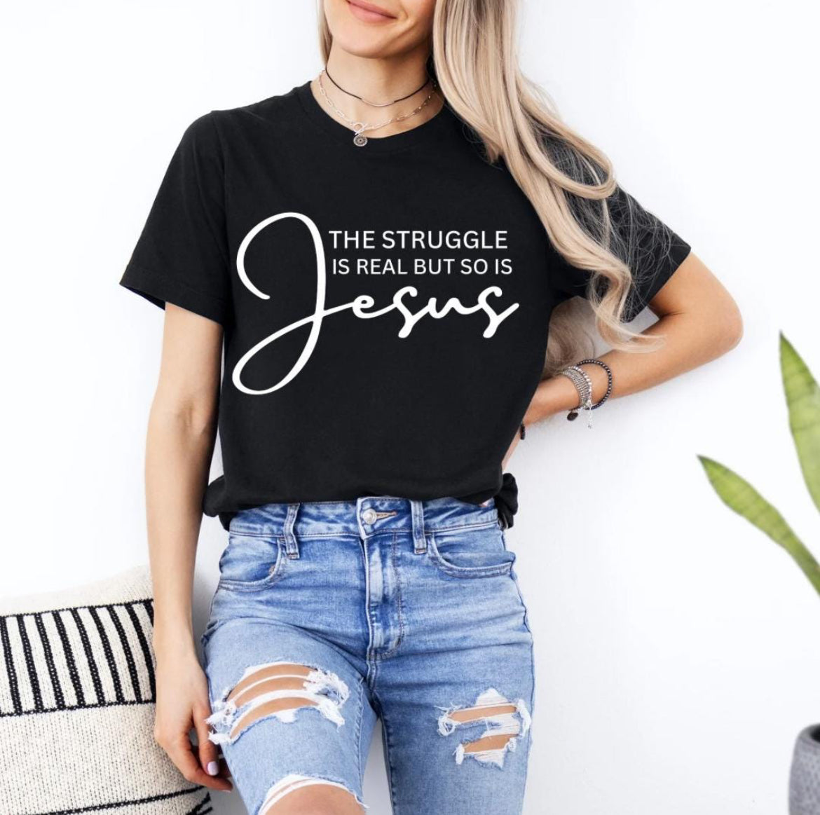 Black crewneck t-shirt that says, “the struggle is real but so is Jesus”.