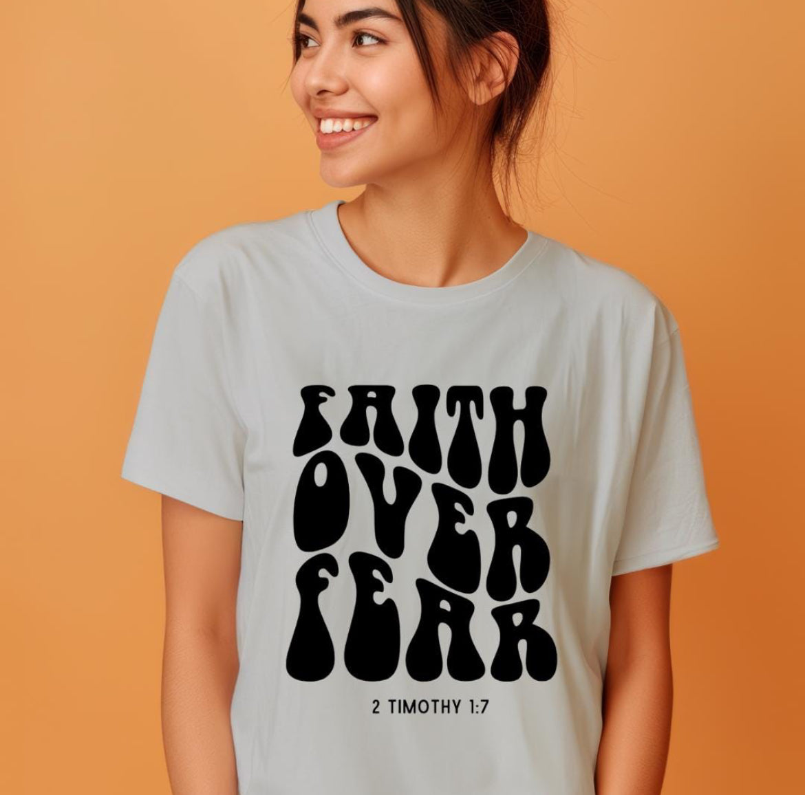 Gray crewneck t-shirt that says “faith over fear” in large bubble letters. Underneath in smaller letters it says, “2 Timothy 1 7.”