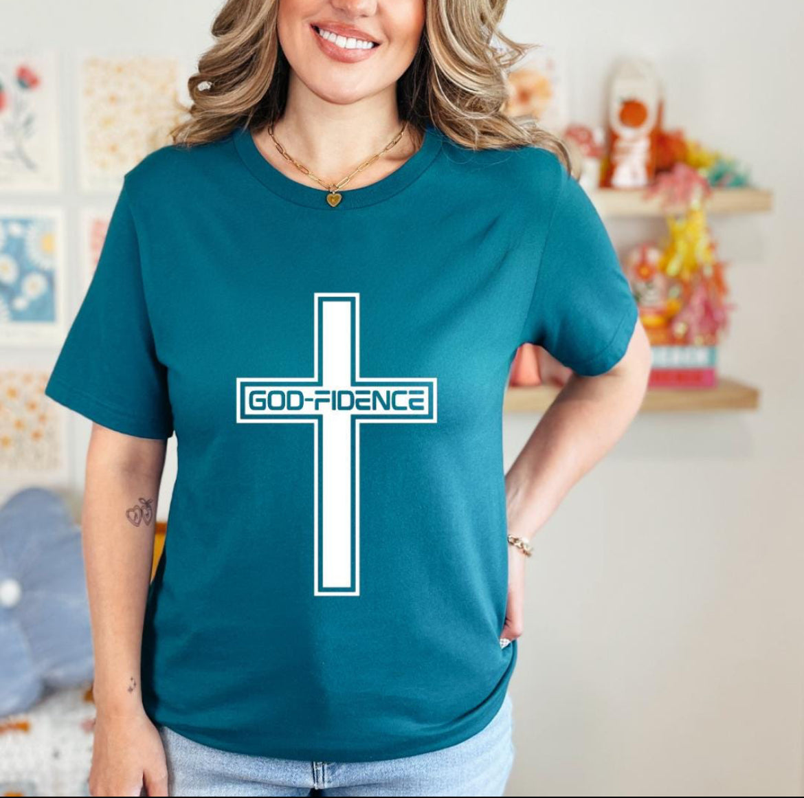 Deep teal crewneck t-shirt that says, “Godfidence” inside of a cross. 