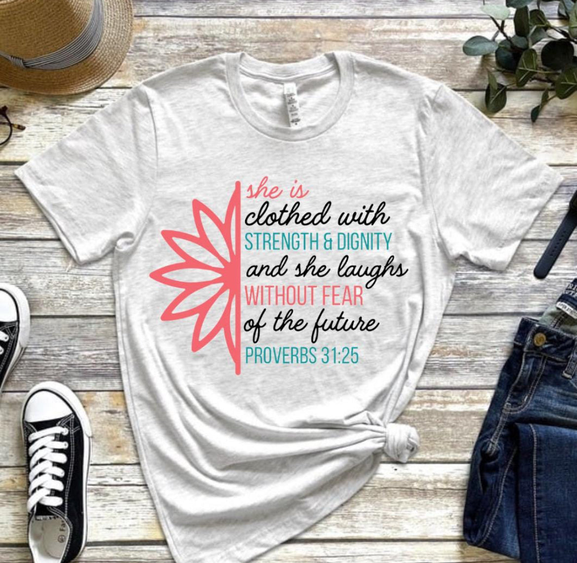 Ash white crewneck t-shirt that says, “she is clothed with strength and dignity and she laughs without fear of the future. Proverbs 31:25.” There is a large flower. The words are peach, teal and white.