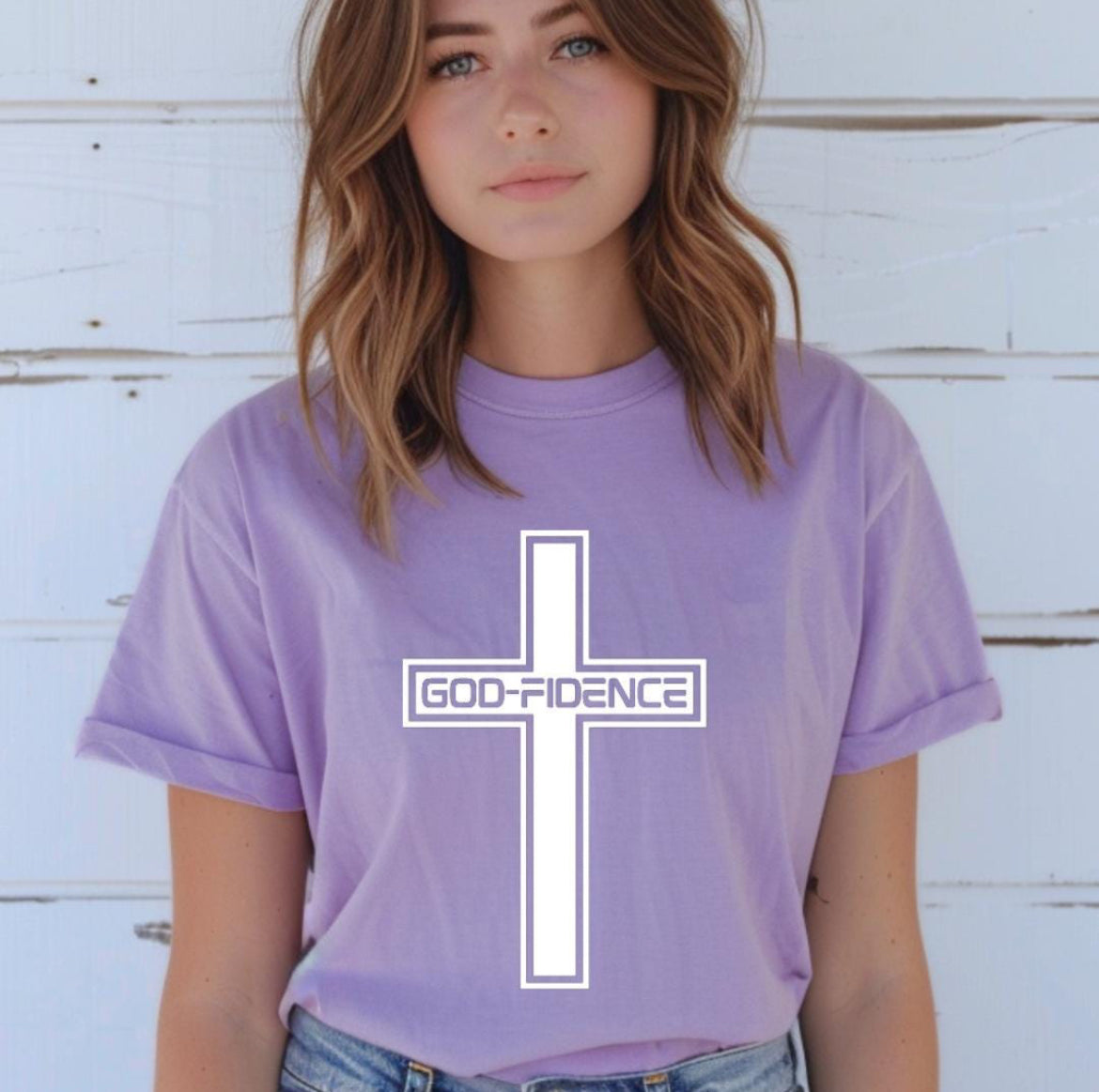 Lavender crewneck t-shirt that says, “Godfidence” inside of a cross. 