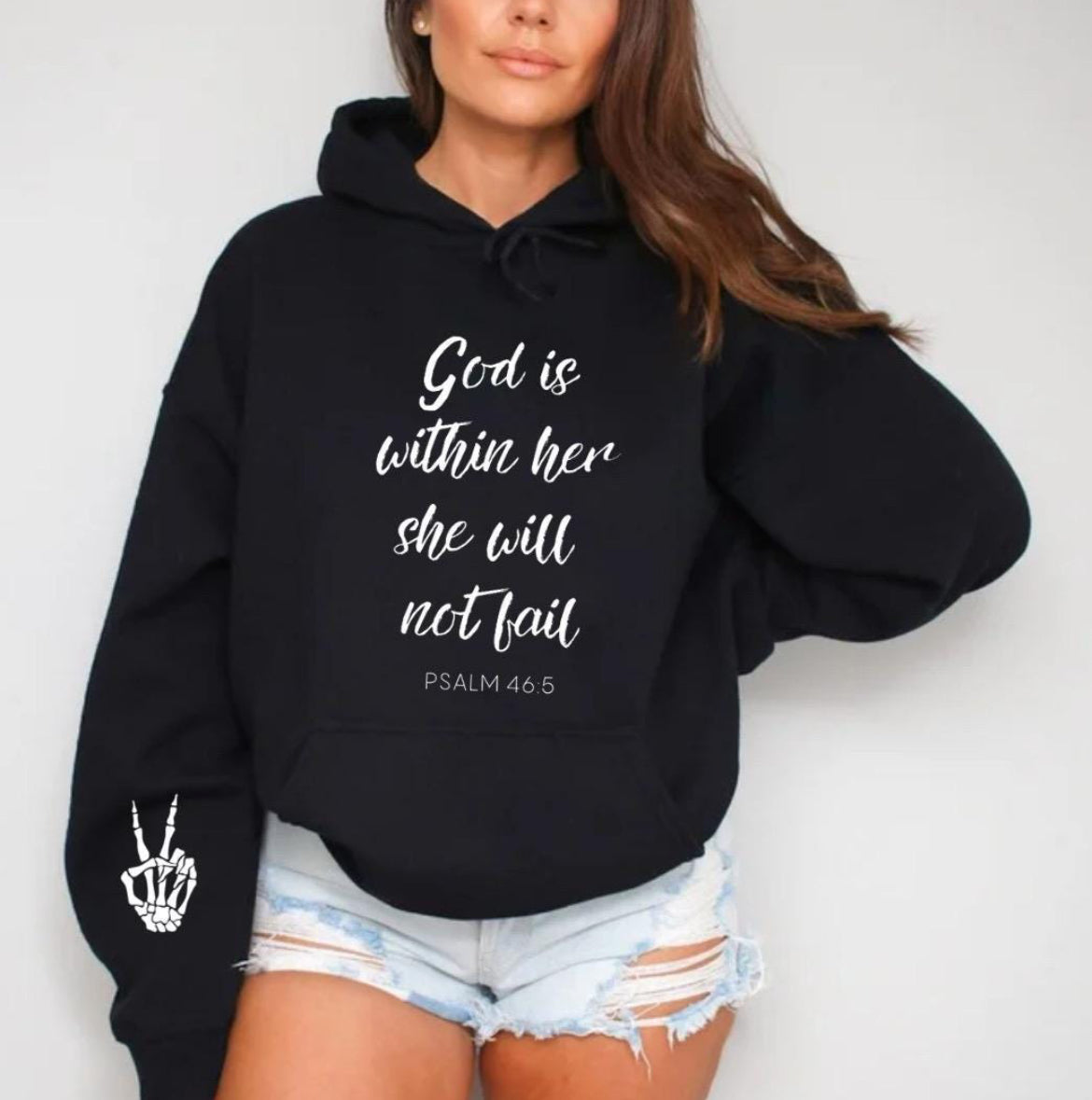 Black hoodie that says, "God is within her she will not fail." Underneath in smaller letters it says, "Psalm 46 5." On the sleeve there is a bones peace sing.