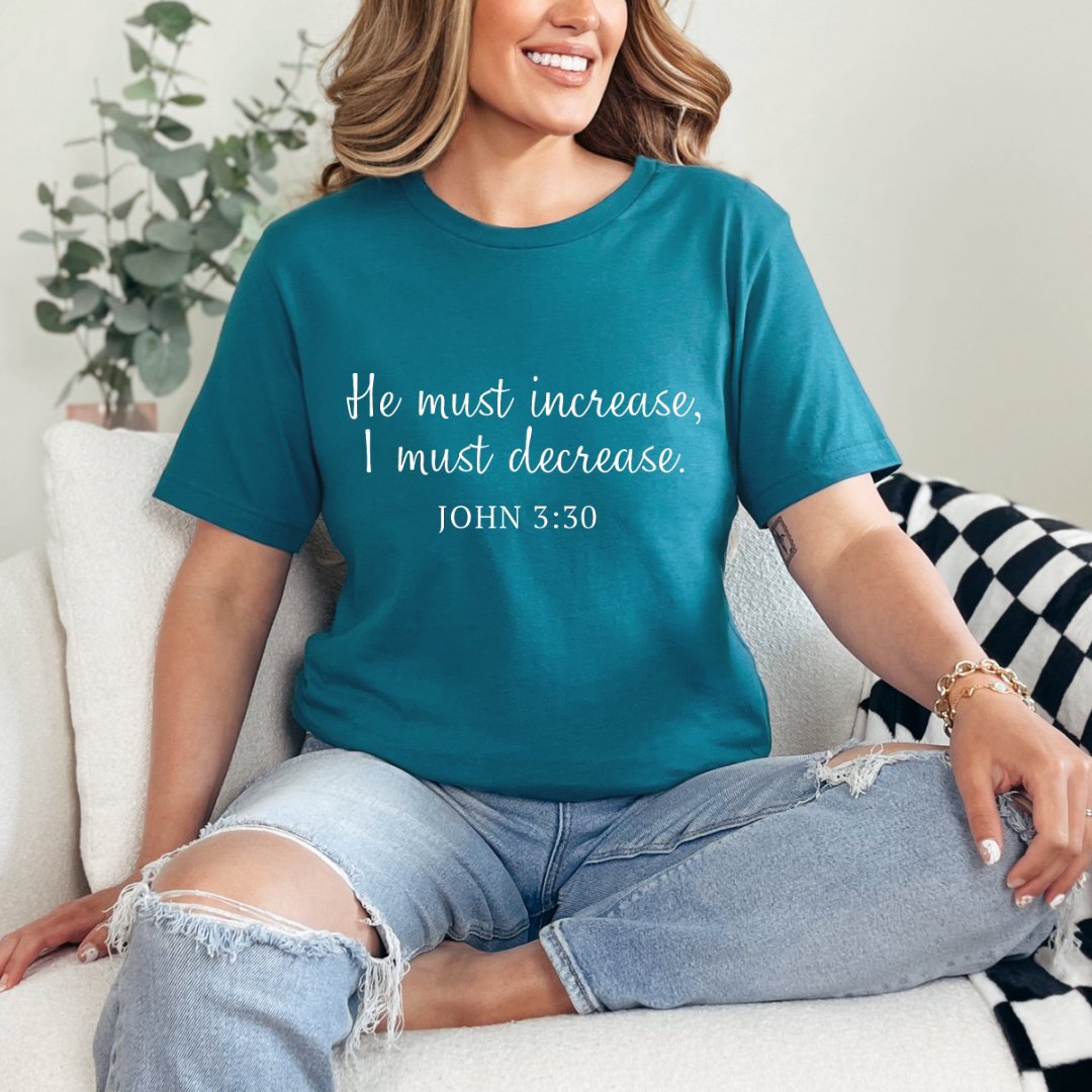 Deep teal crewneck t-shirt that says, “He must increase, I must decrease.” Underneath in smaller letters it says, “John 3 30.”