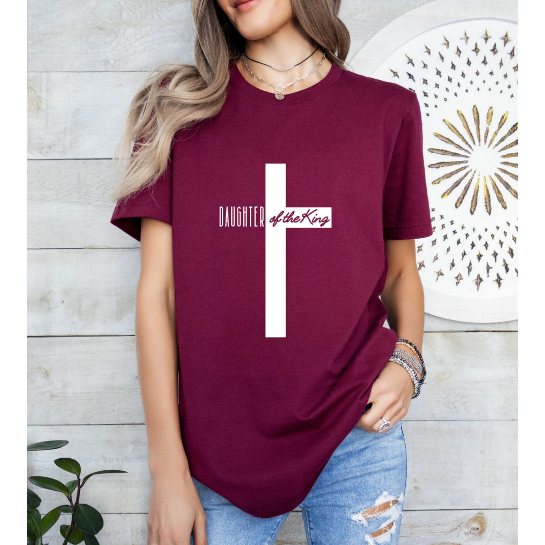 Maroon crewneck t-shirt that says, “Daughter of the King” running through a cross. 