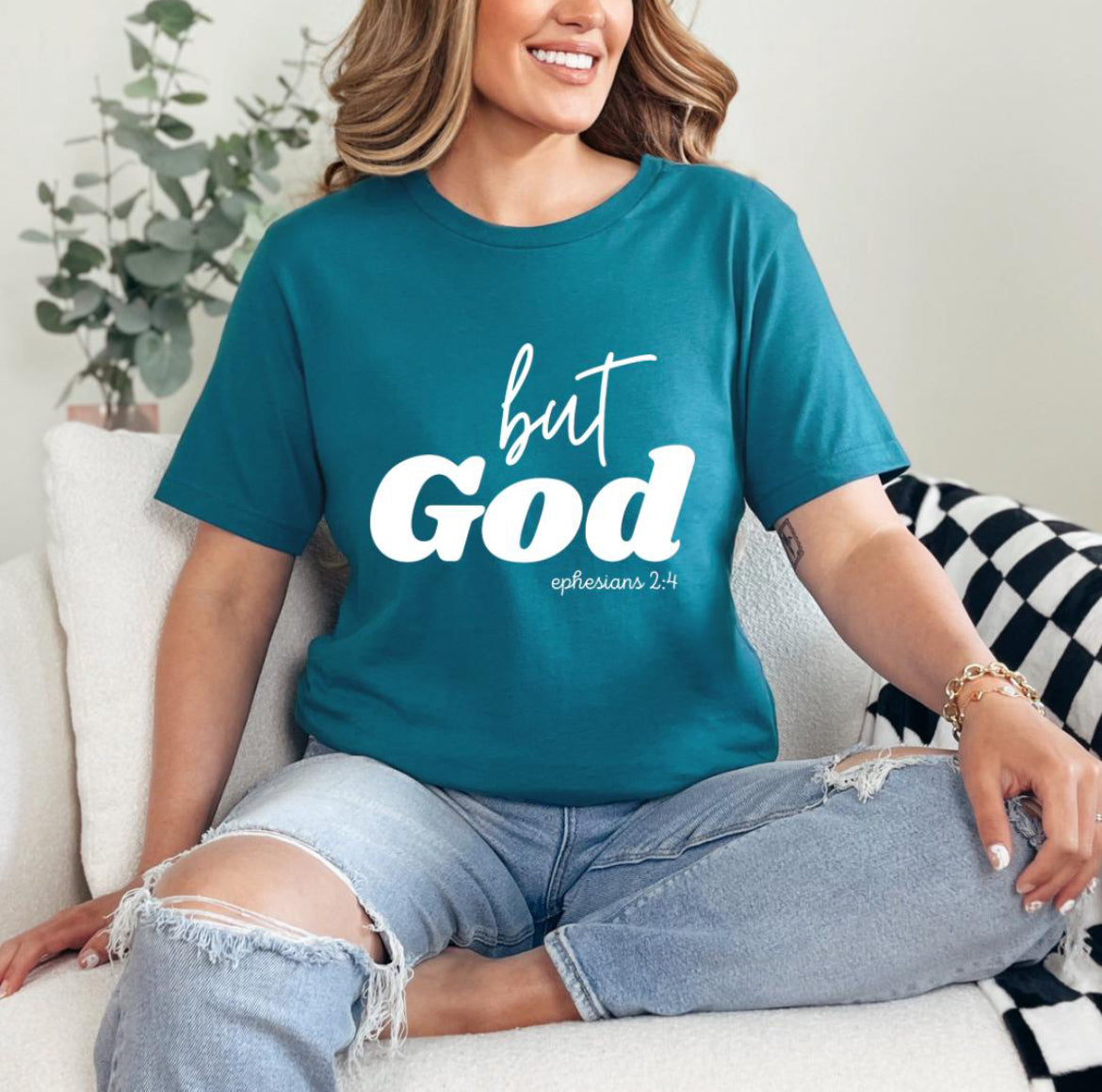 Deep teal crewneck t-shirt that says, “but God” in large letters. Underneath in smaller letters it says, “Ephesians 2 4.”