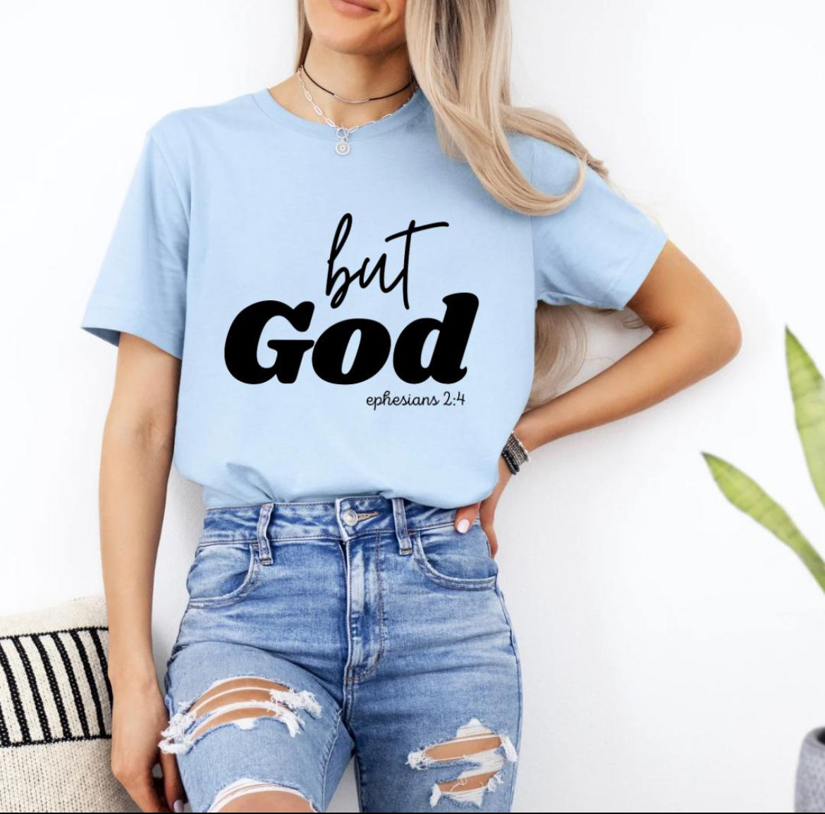 Baby blue crewneck t-shirt that says, “but God” in large letters. Underneath in smaller letters it says, “Ephesians 2 4.”