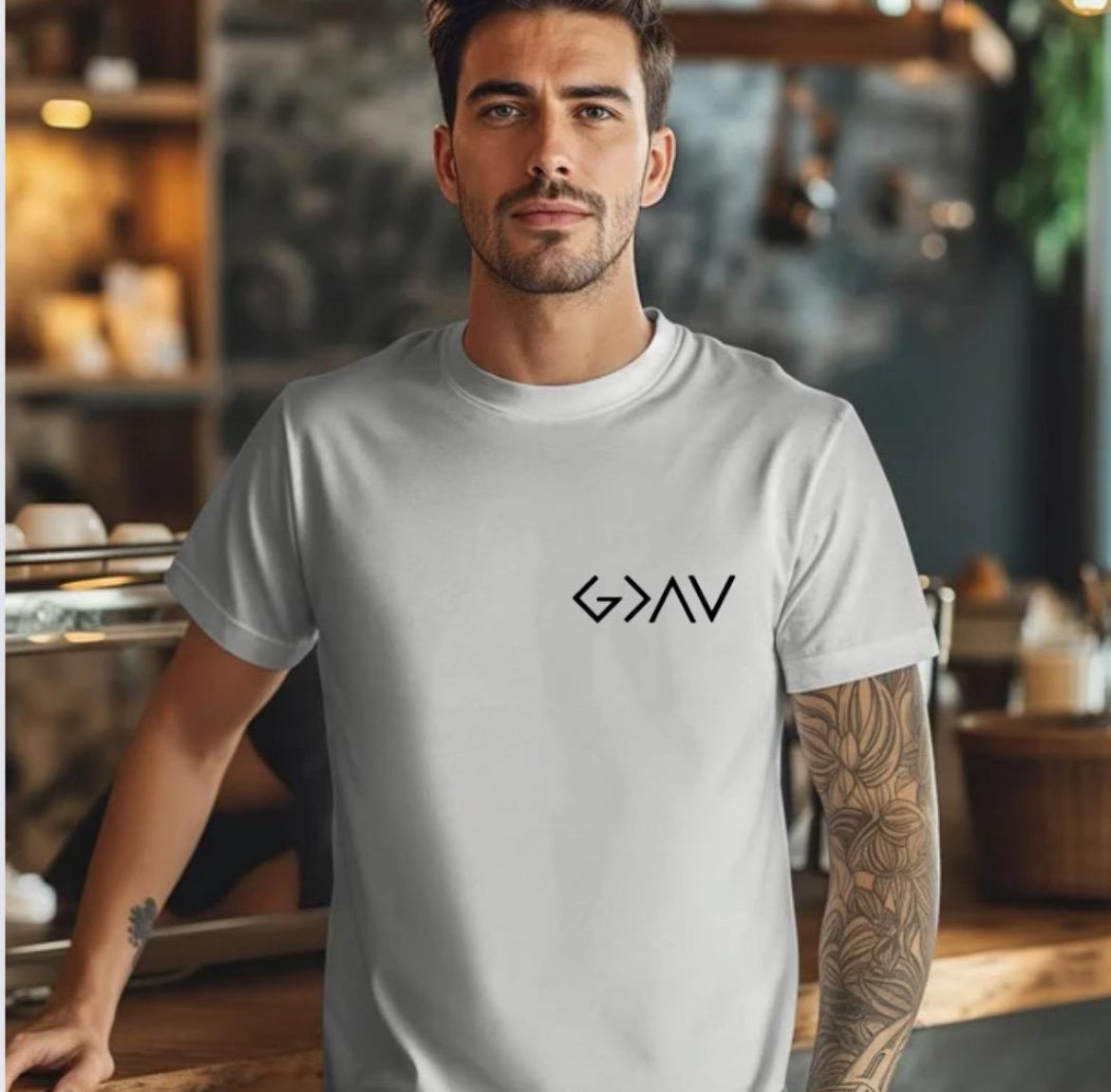 Grey crewneck t-shirt with a cross on the back that has the symbol “God is greater than the highs and lows” as the bottom part of the cross.  The front has the same symbol in the upper left-hand corner.