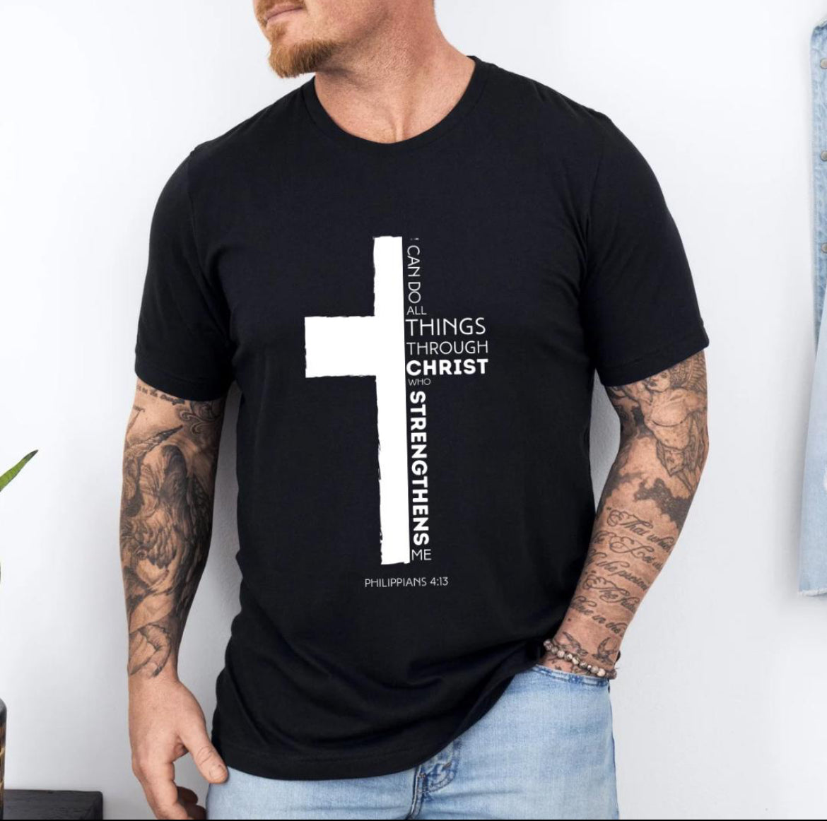 Black crewneck t-shirt with a cross where half of the cross is the Bible verse Philippians 4:13. It says, “I can do all things through Christ who strengthens me.”