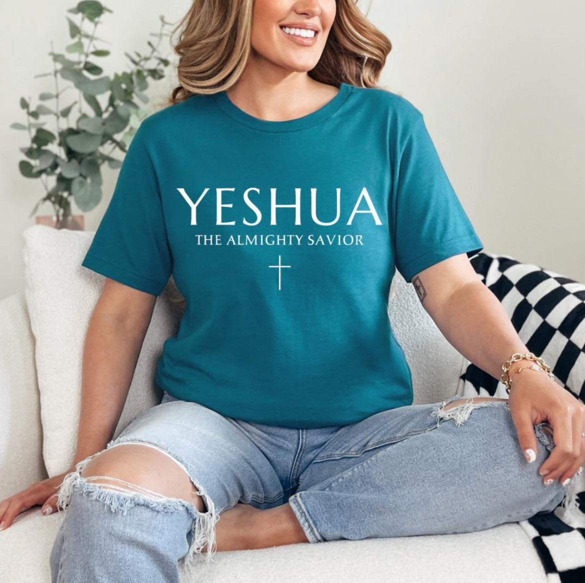 Deep teal Crewneck T-shirt that says, “Yeshua” in large letters. Underneath in smaller letters it says, “the almighty savior” and under that is a small cross. 