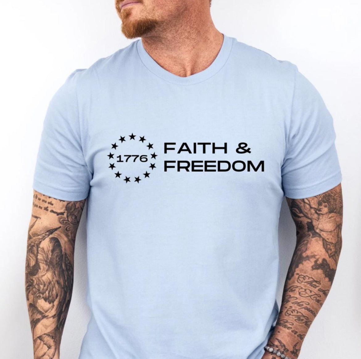 Baby blue crewneck t-shirt that says, “Faith and freedom” with a Betsy Ross flag star symbol and in the middle it says, “1776”.