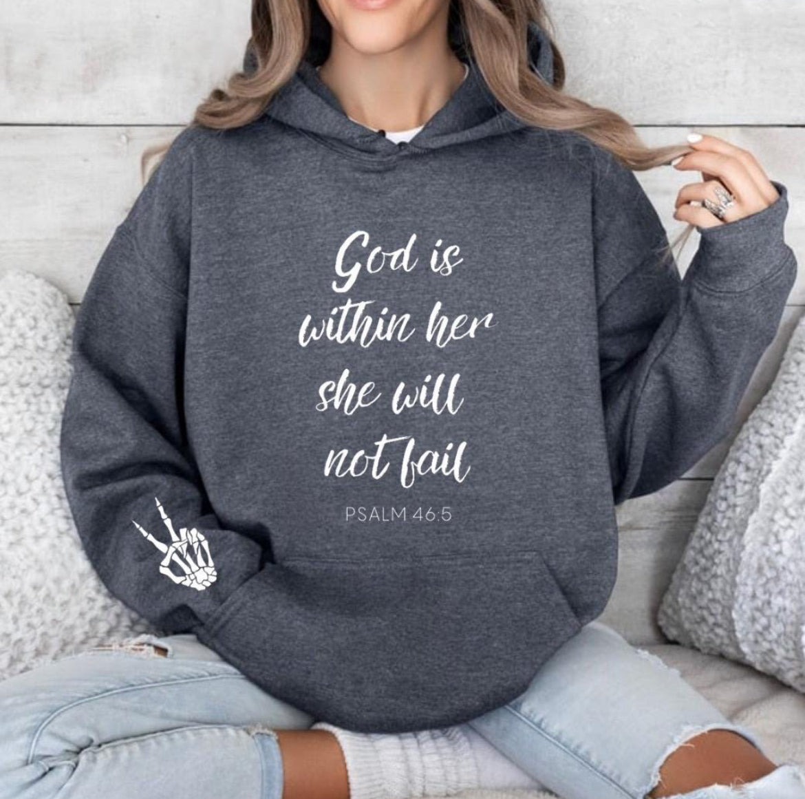 Dark gray hoodie that says, "God is within her she will not fail." Underneath in smaller letters it says, "Psalm 46 5." On the sleeve there is a bones peace sing.