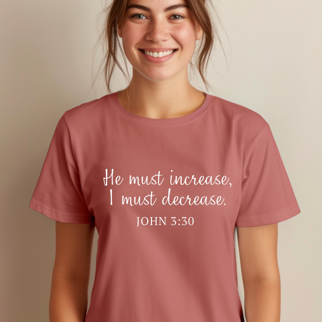 Mauve crewneck t-shirt that says, “He must increase, I must decrease.” Underneath in smaller letters it says, “John 3 30.”