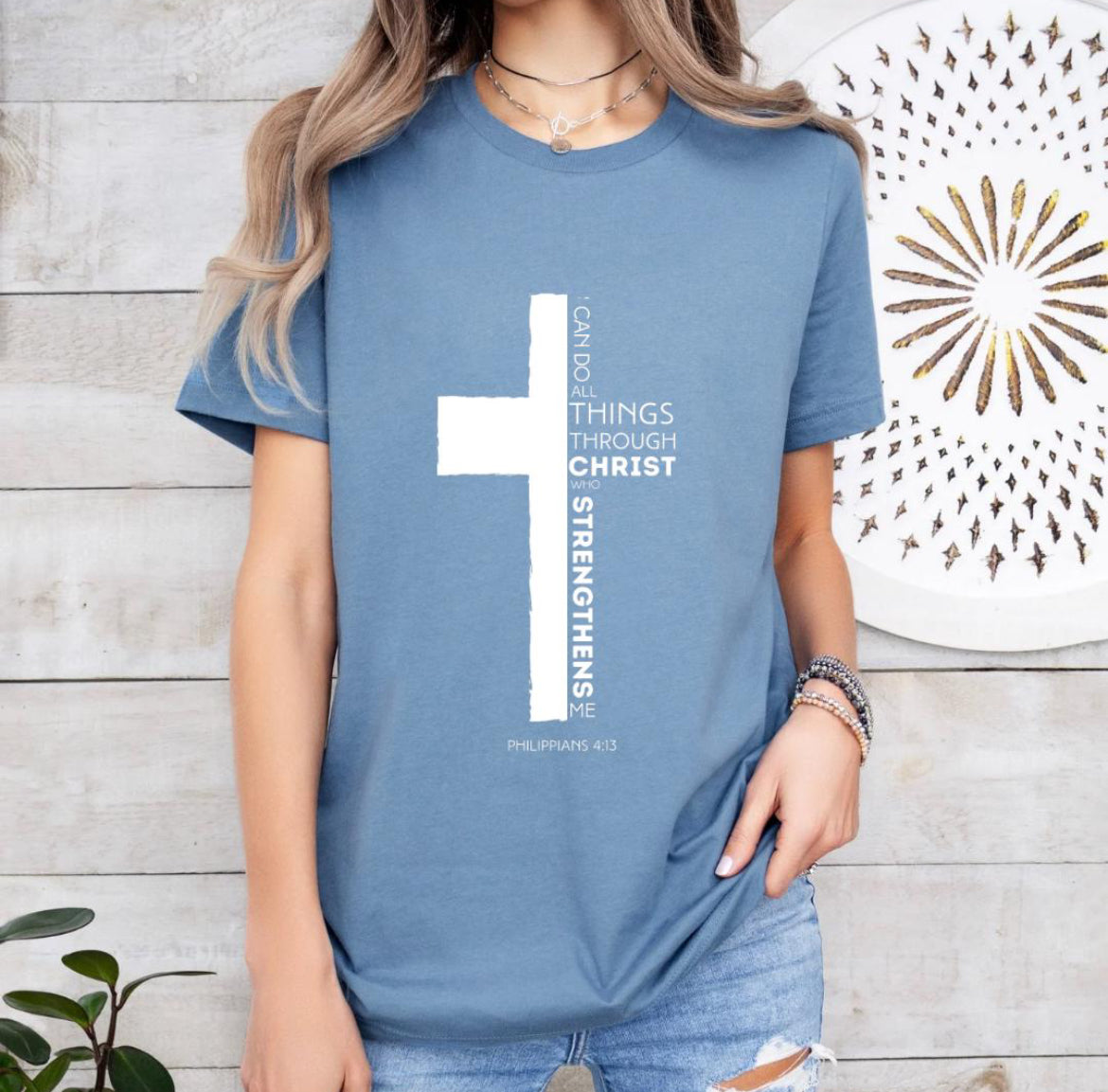 Steel blue crewneck t-shirt with a cross where half of the cross is the Bible verse Philippians 4:13. It says, “I can do all things through Christ who strengthens me.”