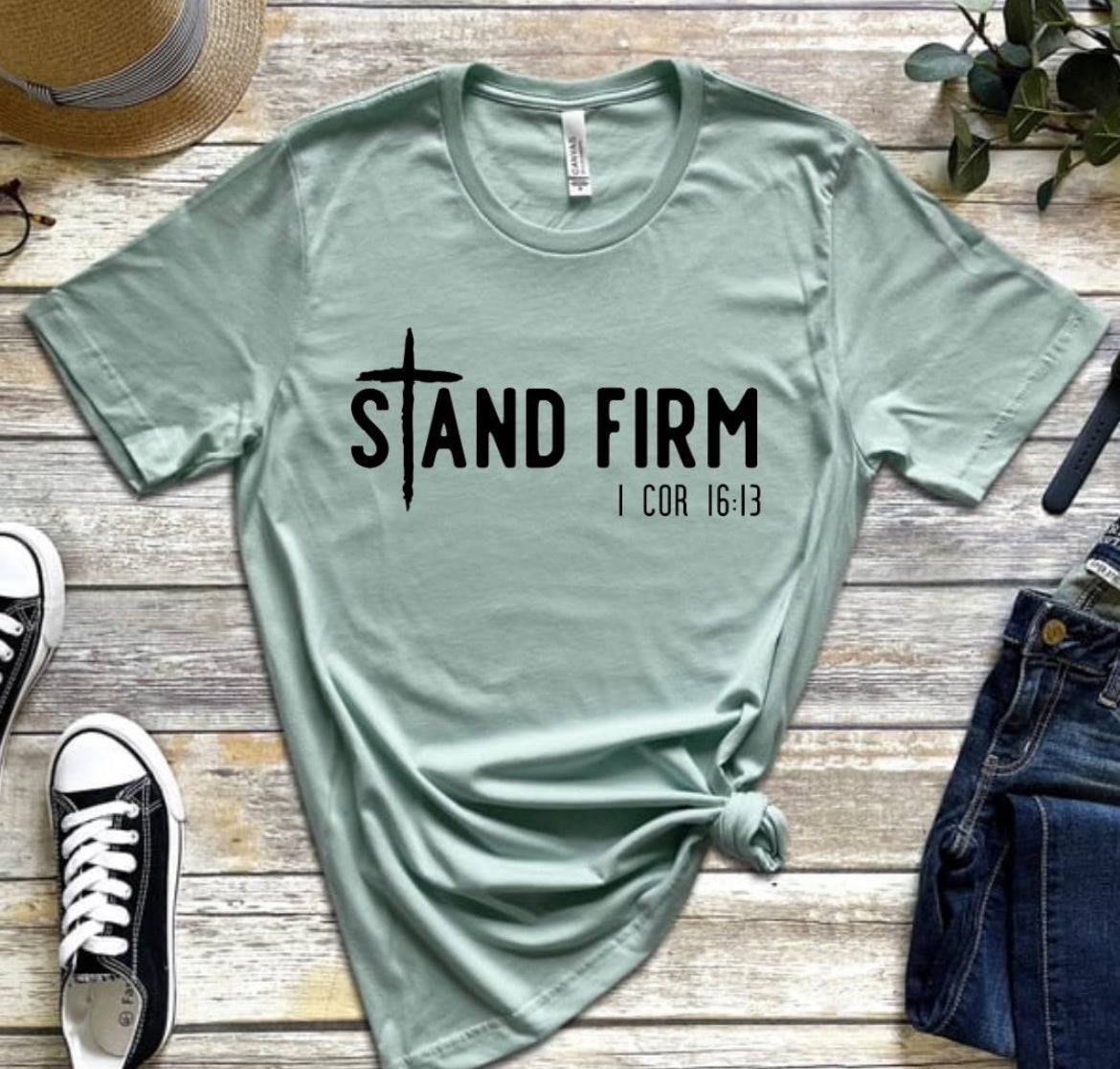 Dusty green shirt that says, “Stand Firm” in large letters. The “t” in stand is a cross. Underneath in smaller letters it says, “1 Corinthians 16:13”.