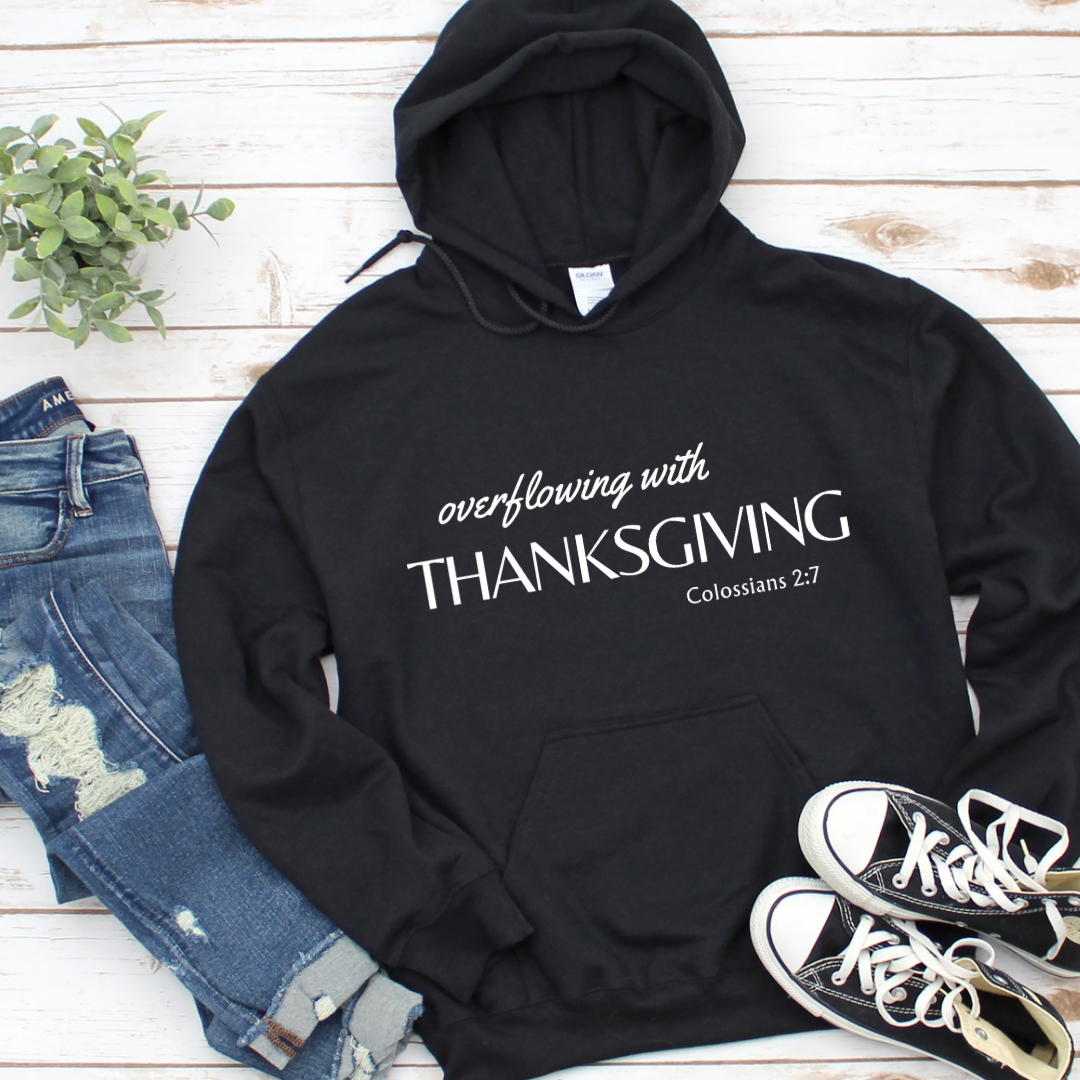 Black hoodie sweatshirt that says, “overflowing with Thanksgiving. Colossians 2:7.”