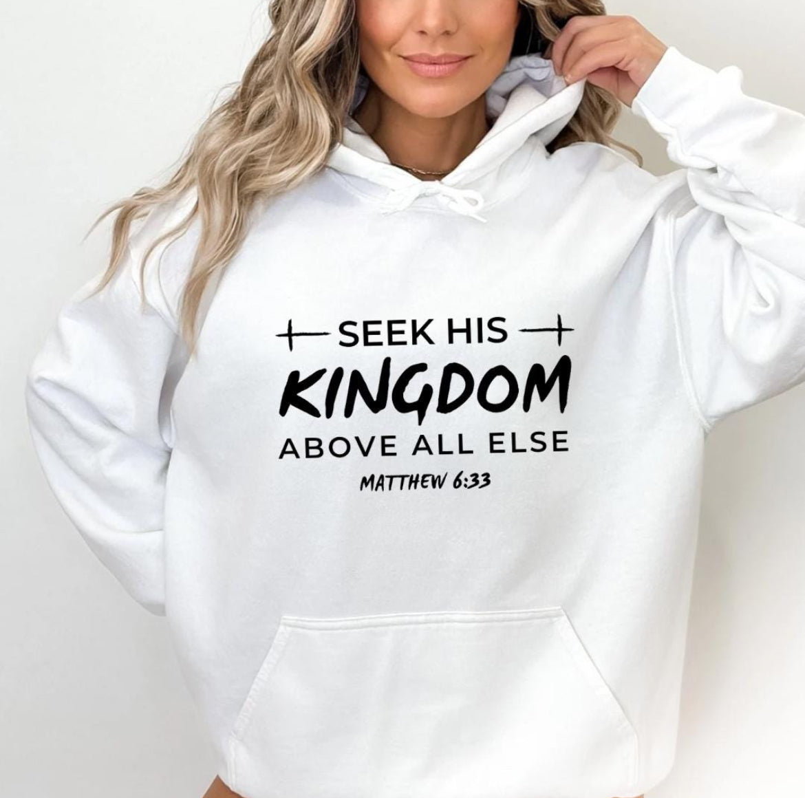 White hoodie that says, "Seek his Kingdom above all else." Underneath in smaller letters it says, "Matthew 6 33." There are two crosses as embellishments.