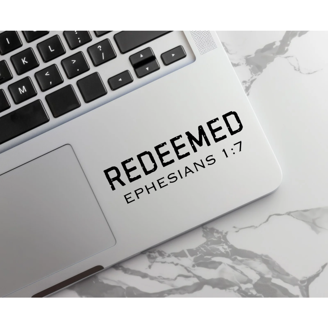 Laptop keyboard sticker decal that says, “Redeemed” in large bold distressed letters. Underneath in smaller capital letters it says, “Ephesians 1 7.”