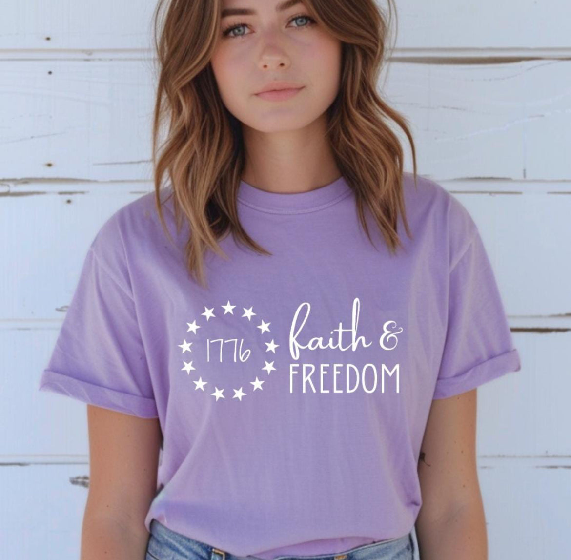 Lavender crewneck t-shirt that says, “Faith and freedom.” There is a Betsy Ross flag stars symbol with “1776” in the middle. 