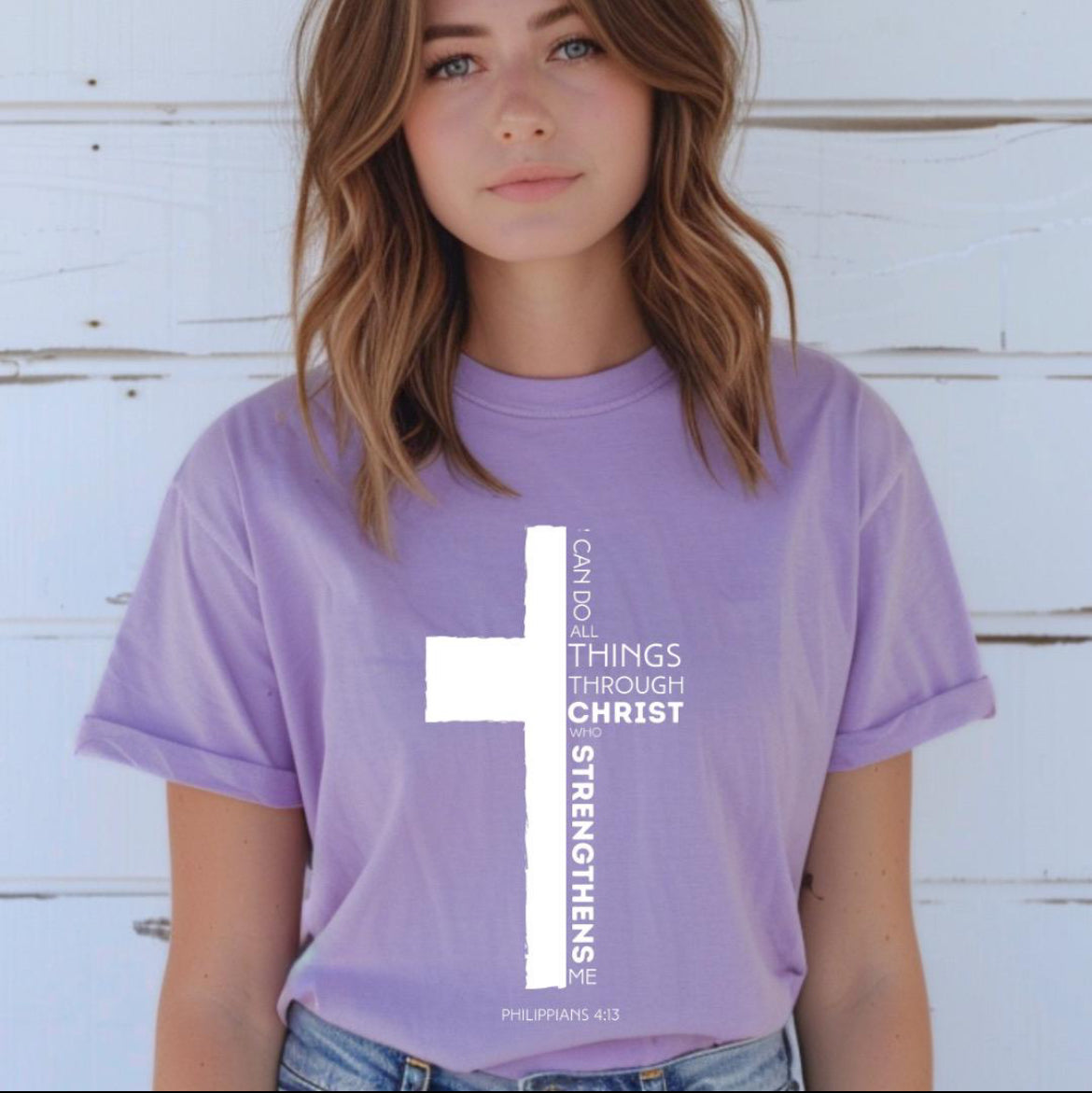 Lavender crewneck t-shirt with a cross where half of the cross is the Bible verse Philippians 4:13. It says, “I can do all things through Christ who strengthens me.”