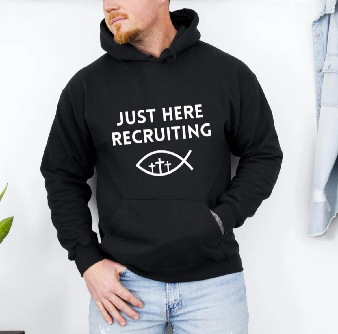 Black hoodie that says, "Just here recruiting" with the ichthus fish symbol with three crosses inside the fish.