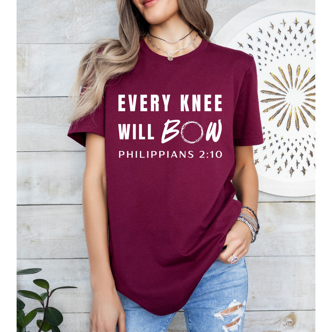 Maroon crewneck t-shirt that says, “every knee will bow. Philippians 2:10” with a crown of thorns as the “o” in bow.