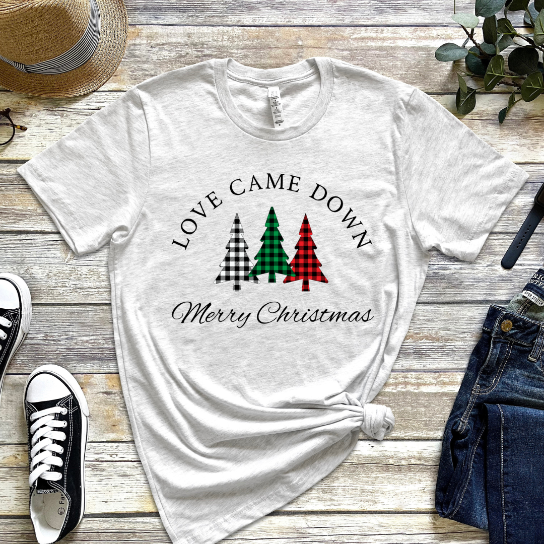 Ash white crewneck t-shirt that says, "Love came down. Merry Christmas." It features 3 Christmas trees in buffalo plaid green, red and white.