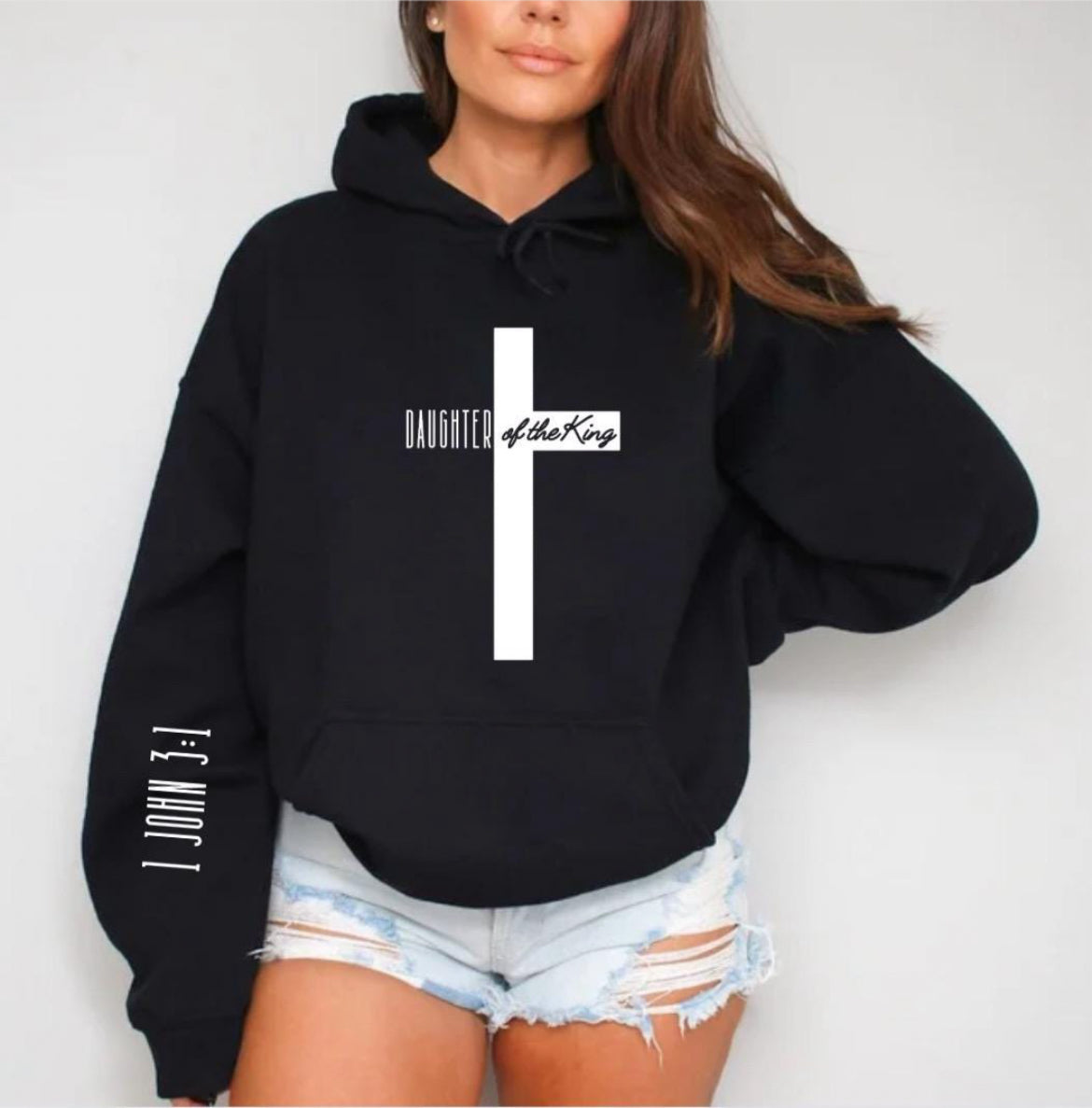 Black hooded sweatshirt with a large cross that says, "Daughter of the King," On the sleeve it says, "1 John 3:1."