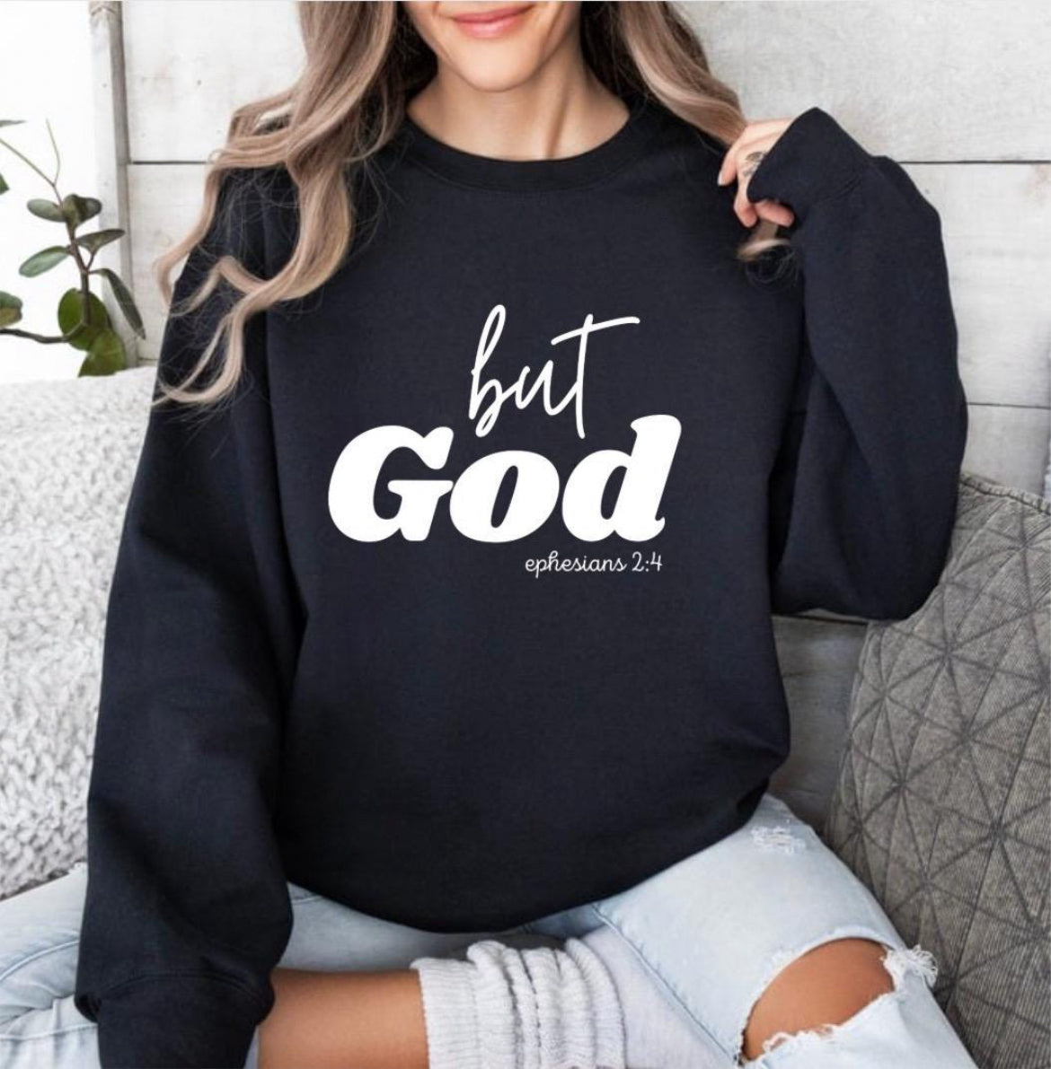 Black crewneck sweatshirt that says, "But God" in large letters. Underneath it says, "Ephesians 2 verse 4" in smaller letters. 