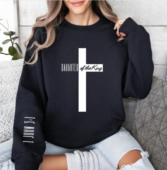 Black crewneck sweatshirt with a large cross that says, "Daughter of the King," On the sleeve it says, "1 John 3:1."