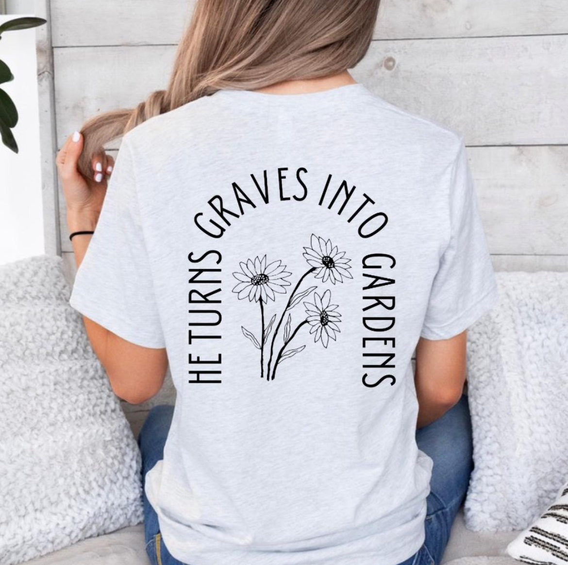 Ash white crewneck t-shirt back that says, “He turns graves into gardens.” The words in the shape of a grave with flowers in the middle. 