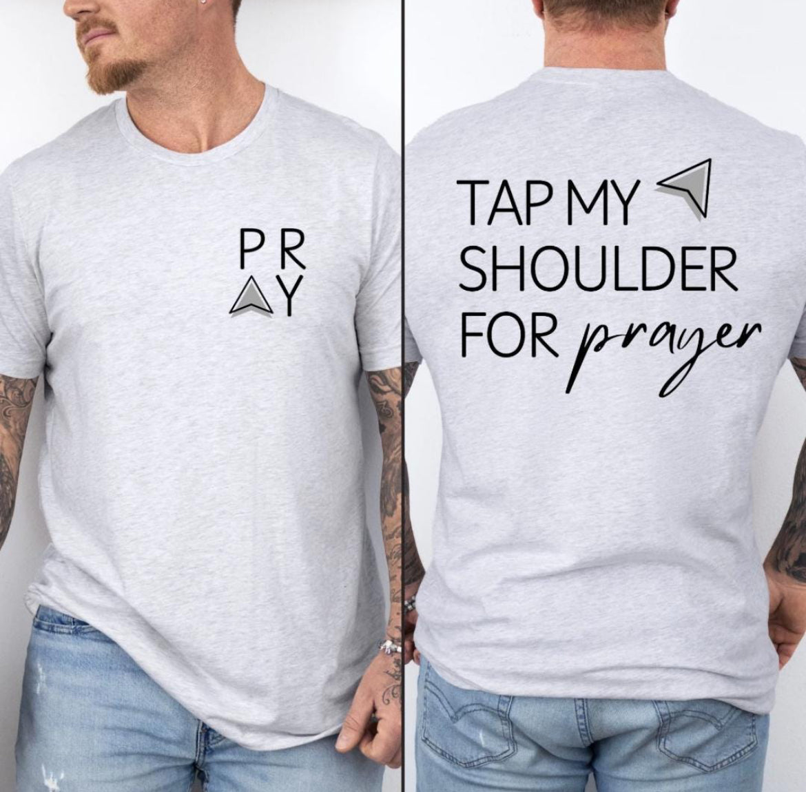 Ash white Crewneck t-shirt that says, “tap my shoulder for prayer” with an aesthetic arrow pointing to the shoulder. On the front of the shirt it says, “PRAY” up in the left-hand corner of the shirt. 