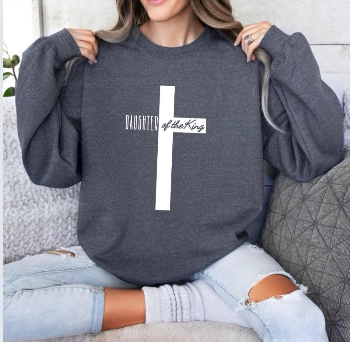 Dark gray heather crewneck sweatshirt with a large cross that says, "Daughter of the King," On the sleeve it says, "1 John 3:1."