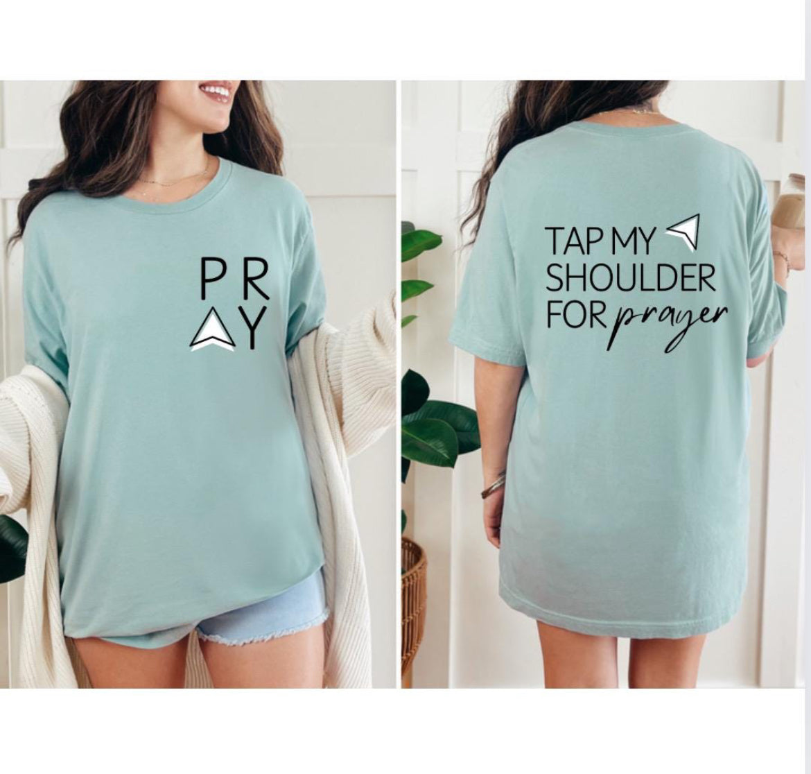 Dusty green Crewneck t-shirt that says, “tap my shoulder for prayer” with an aesthetic arrow pointing to the shoulder. On the front of the shirt it says, “PRAY” up in the left-hand corner of the shirt. 