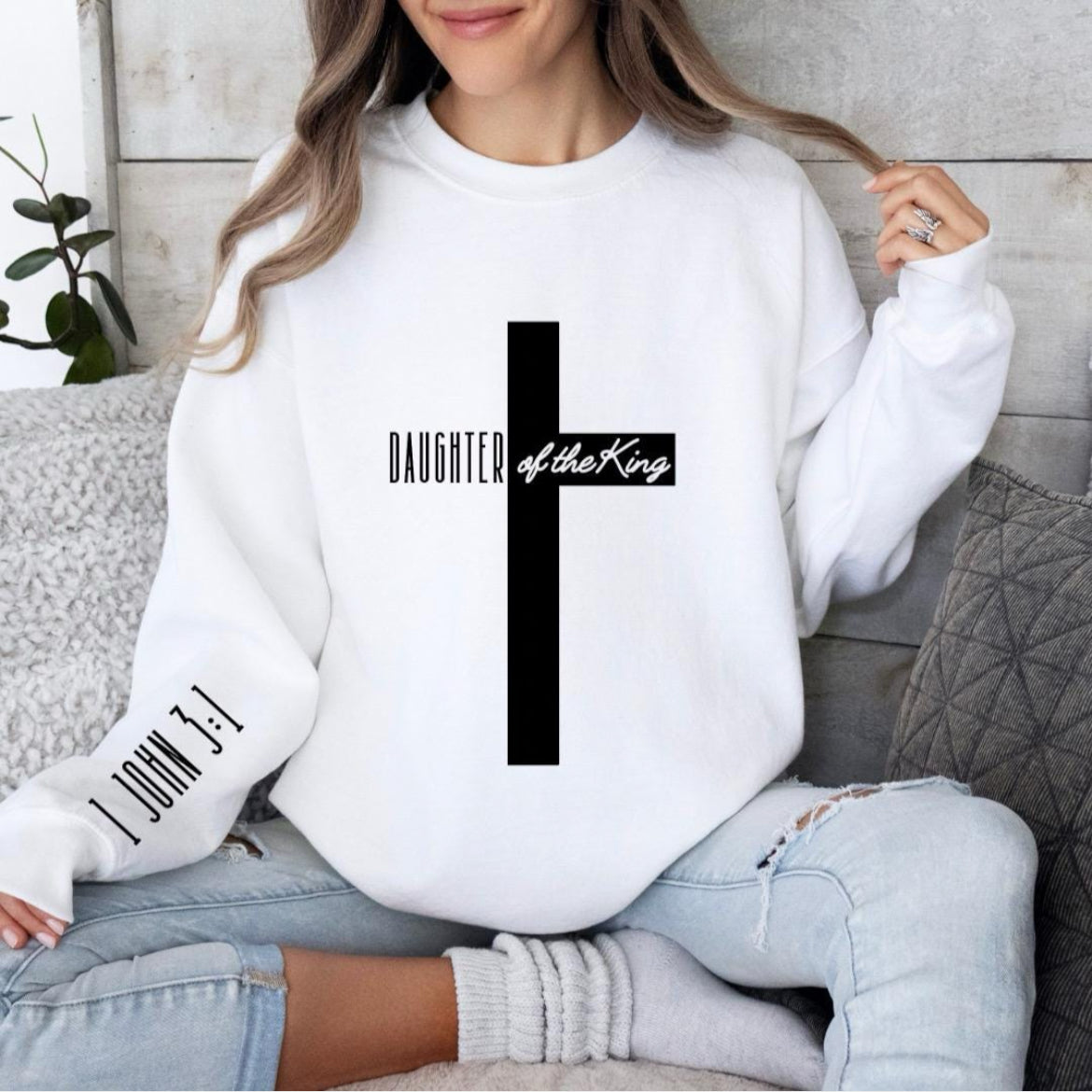 white crewneck sweatshirt with a large cross that says, "Daughter of the King," On the sleeve it says, "1 John 3:1."