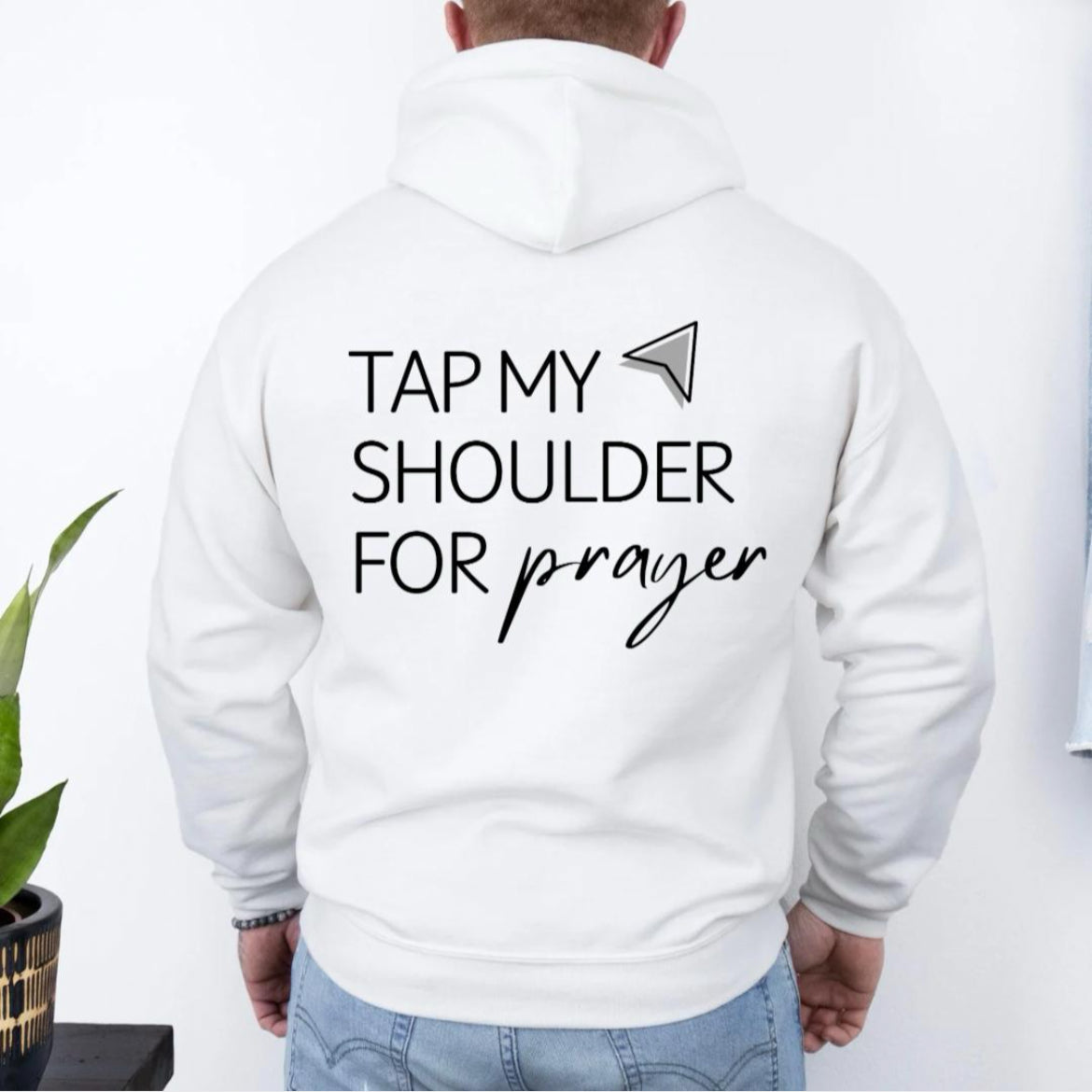 Back of dark white hoodie sweatshirt that has an aesthetic arrow pointing towards the shoulder that says, "Tap my shoulder for prayer."