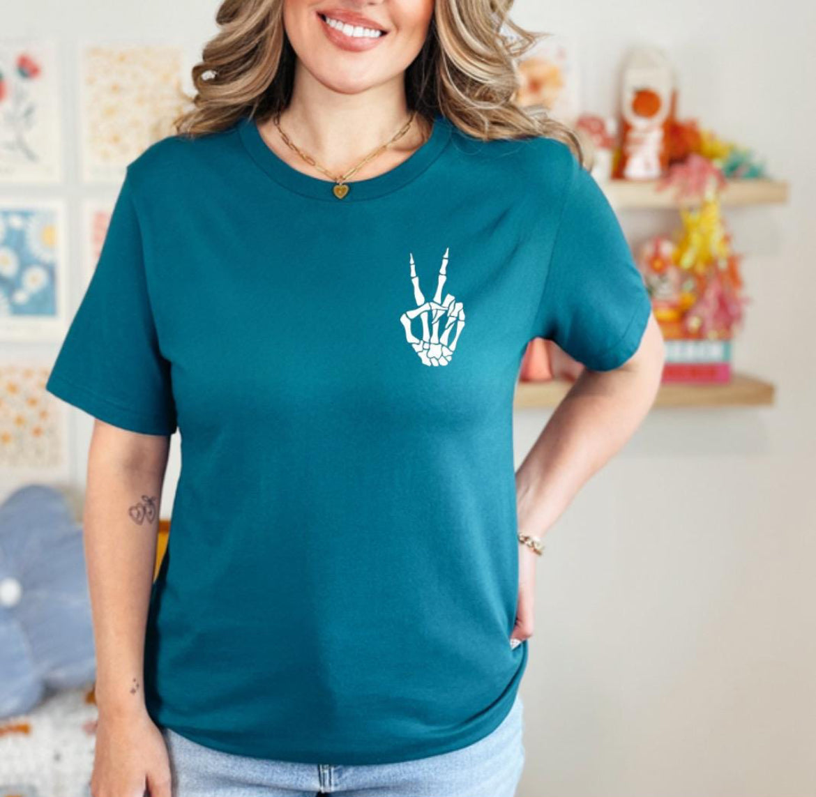 Deep teal crewneck t-shirt that has a small bones hand peace sign in the upper left-hand corner. 