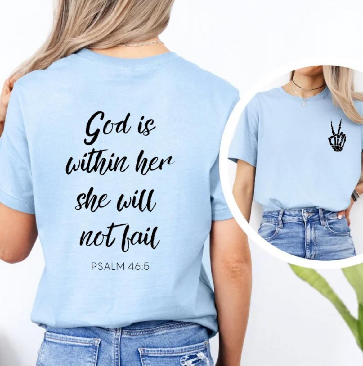 Baby blue crewneck t-shirt back that says, “God is within her she will not fail.” Underneath in smaller letters it says, “Psalm 46 5.” The front has a small bones hand peace sign in the upper left-hand corner. 