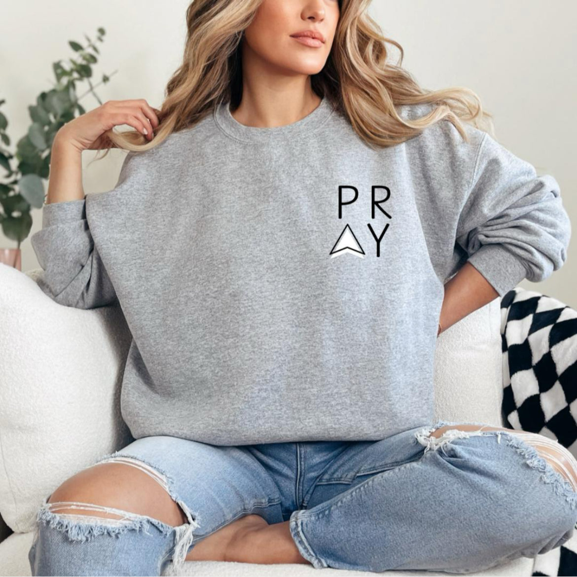 Light grey crewneck sweatshirt that says, "PRAY" where the A is an arrow in the front left-hand corner of the hoodie.