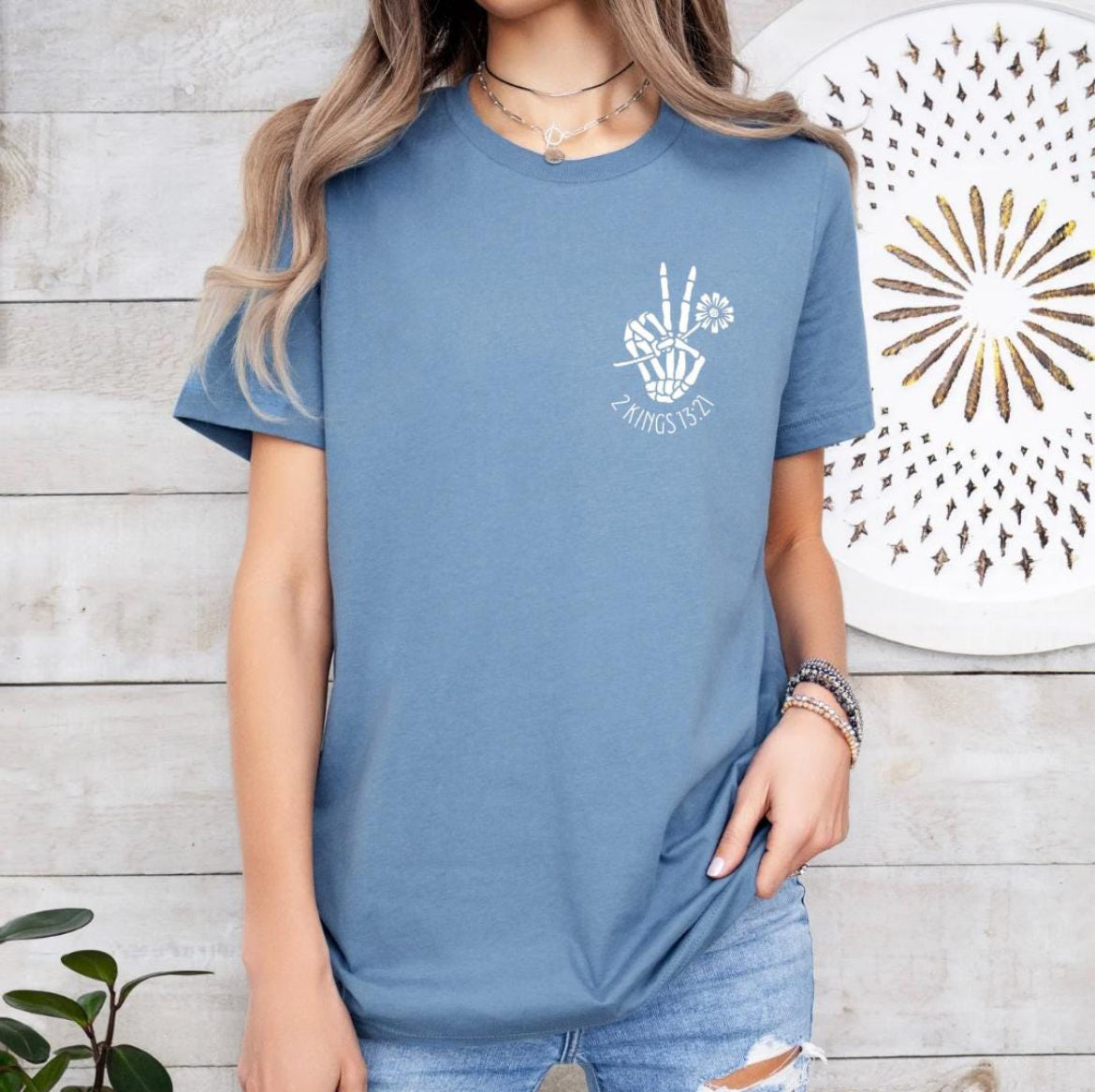 Steel blue crewneck t-shirt that has a bones hand peace sign holding a flower. Underneath it says, “2 Kings 13 21.”