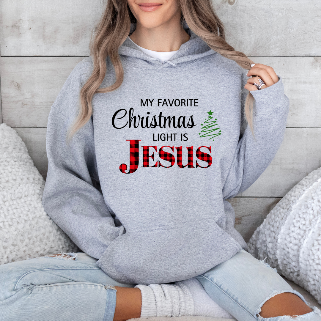 Gray hoodie sweatshirt that says, "My favorite Christmas light is Jesus." Jesus is in buffalo plaid red with a green Christmas tree graphic.