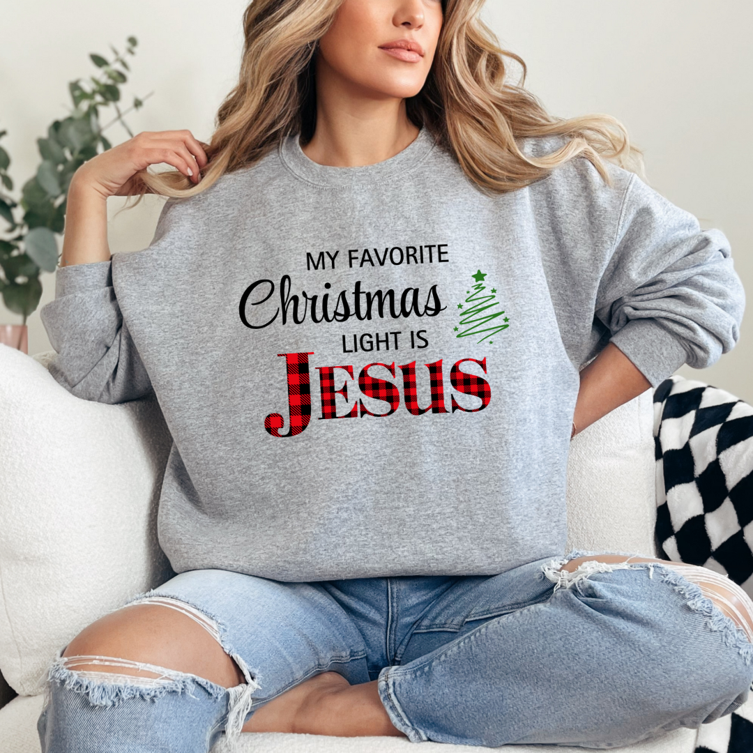 Gray crewneck sweatshirt that says, "My favorite Christmas light is Jesus." Jesus is in buffalo plaid red with a green Christmas tree graphic.