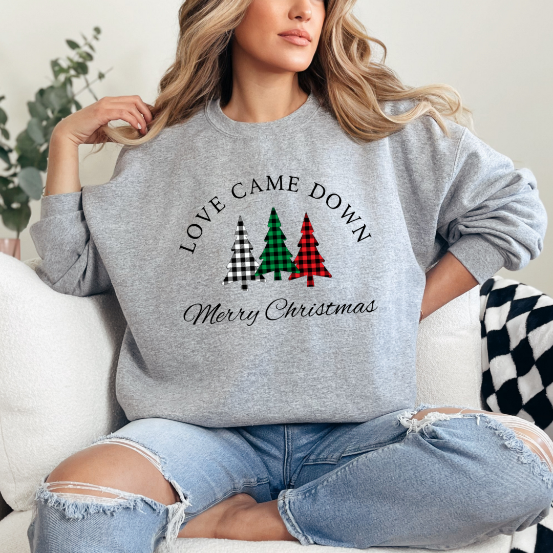 Grey crewneck sweatshirt that says, "Love came down. Merry Christmas" with three Christmas trees in buffalo plaid green, red and black. 