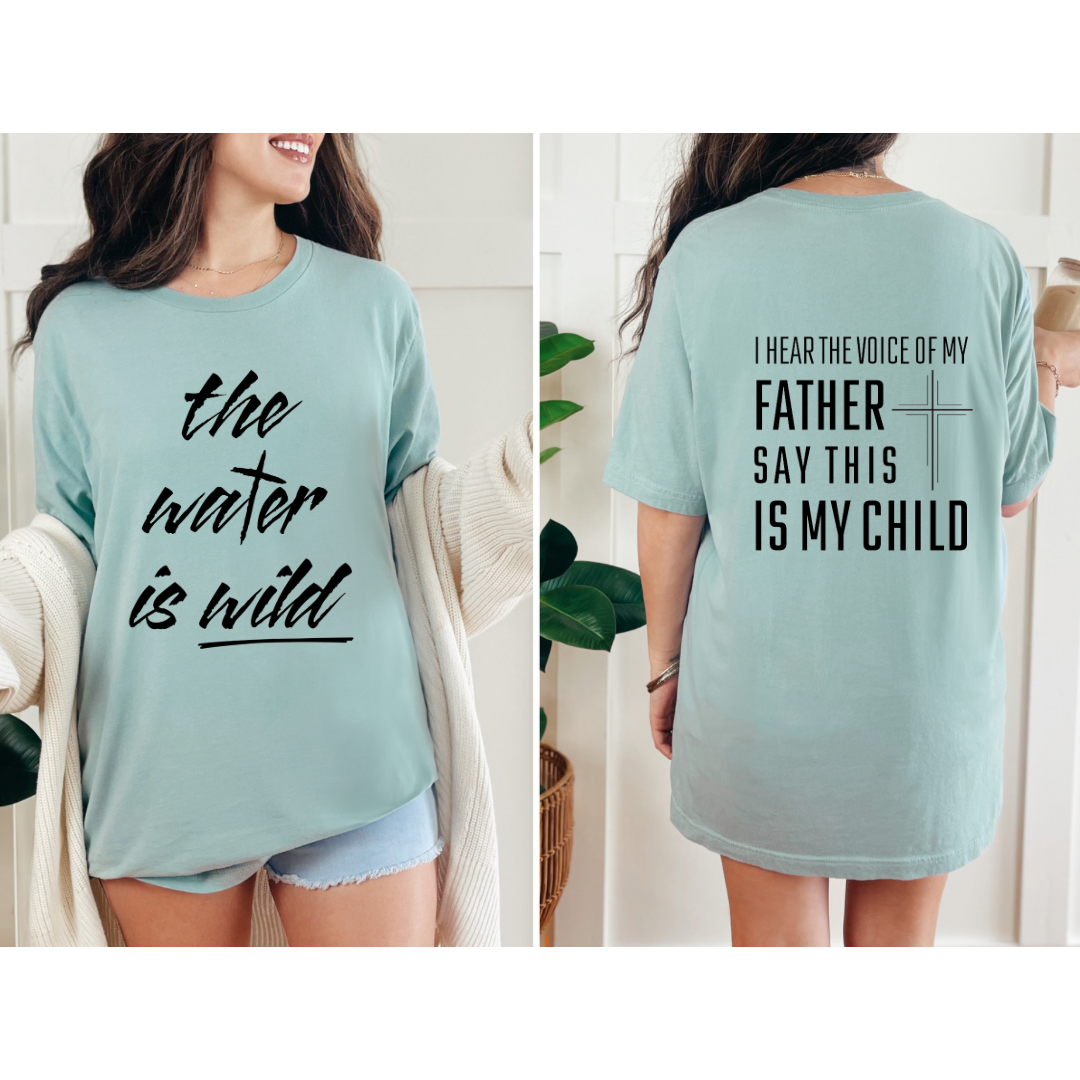 Dusty green crewneck t-Shirt that says, “the water is wild”. The “t” in water is a cross. The back says, “I hear the voice of my father say this is my child” with a large cross in the middle.